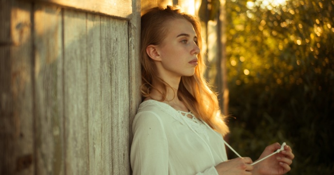 A woman leaning against the side of a wooden building